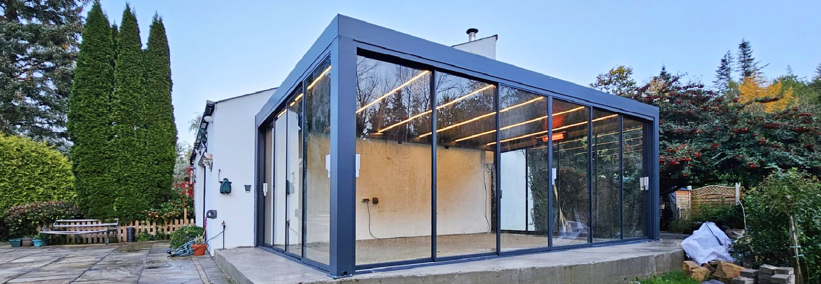 Pergola with glass doors and integrated roof lighting beside a home